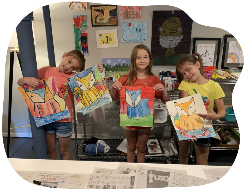 Three children holding up paintings in front of a mirror.